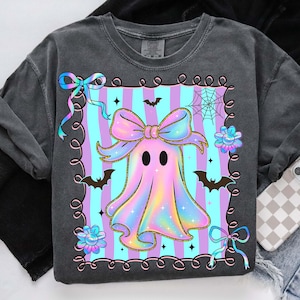 Puede incluir: Una sudadera gris oscuro con un dise&ntilde;o de fantasma pastel. El fantasma tiene un gran lazo y est&aacute; rodeado de murci&eacute;lagos, flores y una telara&ntilde;a. El fondo tiene rayas verticales azules y moradas.