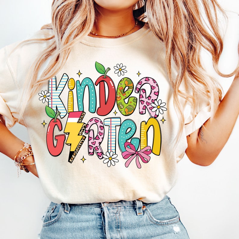 May include: A white t-shirt with a colorful graphic that says "Kindergarten" with a variety of patterns and designs, including hearts, stars, and a lightning bolt.