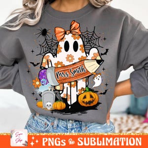 Puede incluir: Una sudadera gris con un fantasma sosteniendo un l&aacute;piz que dice "Mrs. Smith". El fantasma est&aacute; rodeado de flores naranjas y amarillas, una telara&ntilde;a, murci&eacute;lagos y calabazas.