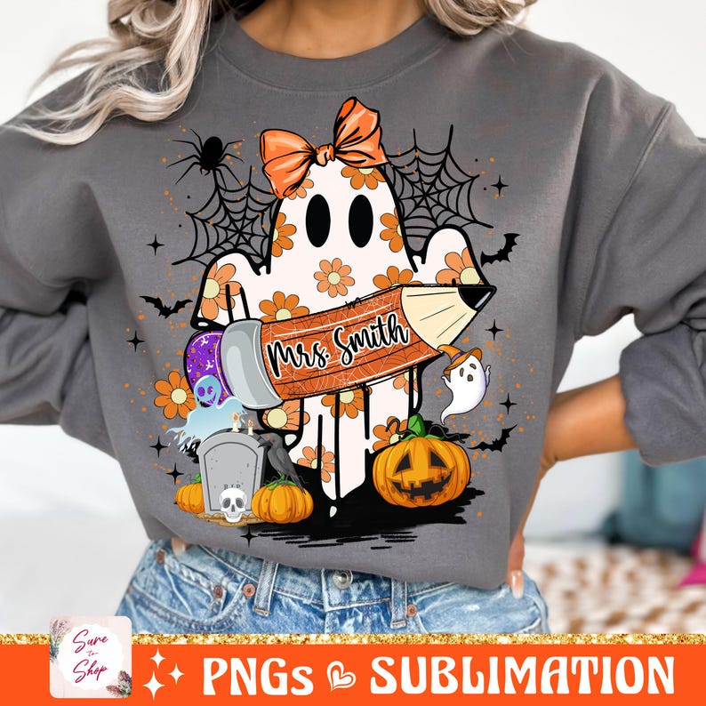 Puede incluir: Una sudadera gris con un fantasma sosteniendo un l&aacute;piz que dice "Mrs. Smith". El fantasma est&aacute; rodeado de flores naranjas y amarillas, una telara&ntilde;a, murci&eacute;lagos y calabazas.
