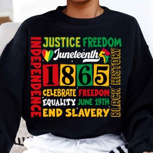 May include: Black sweatshirt with a graphic design featuring the words "Justice Freedom Independence Celebrate Freedom Equality June 19th End Slavery Black History" and the year "1865" in a colourful block design.