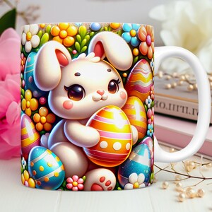 May include: White ceramic mug featuring a colourful illustration of a white bunny holding a yellow, pink and orange Easter egg. The bunny is surrounded by flowers and other Easter eggs in shades of blue, green and purple.
