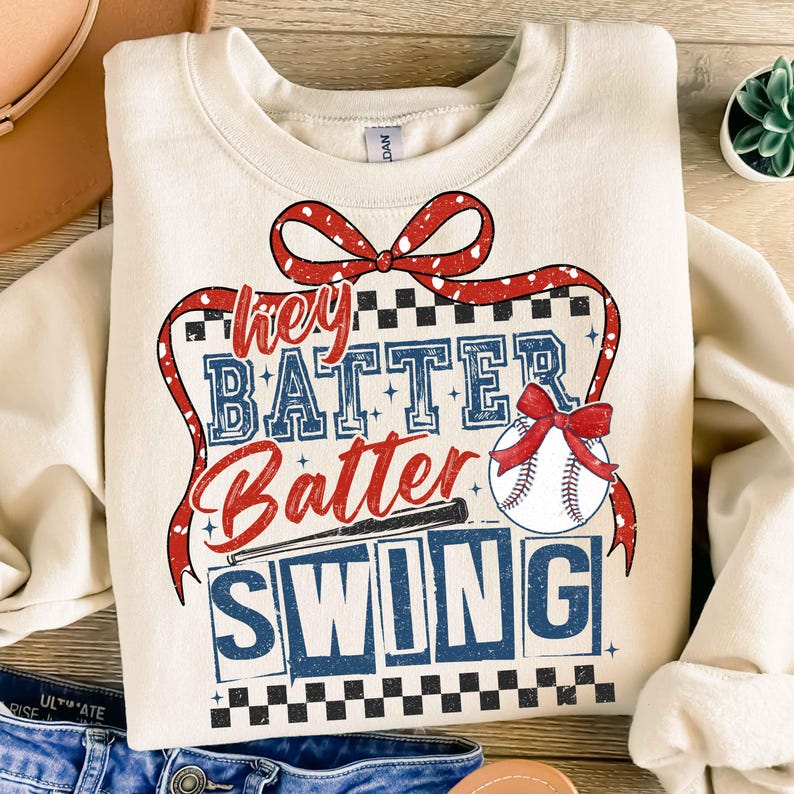 May include: A beige sweatshirt with a red, white, and blue graphic design that says "Hey Batter Batter Swing" with a baseball and bat.