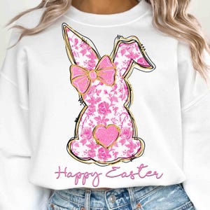 Op de afbeelding: Wit sweatshirt met een roze bloemenkonijn met een gouden strik en een roze hart. De tekst "Happy Easter" is onder het konijn gedrukt.
