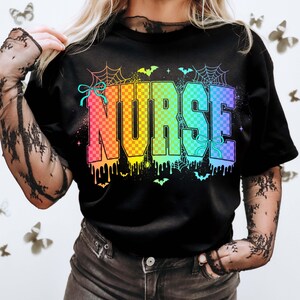 Pu&ograve; includere: T-shirt nera con la scritta "NURSE" in lettere a scacchi arcobaleno. Il design include ragnatele, pipistrelli e vernice che gocciola, creando un tema di Halloween. La maglietta ha uno scollo tondo.