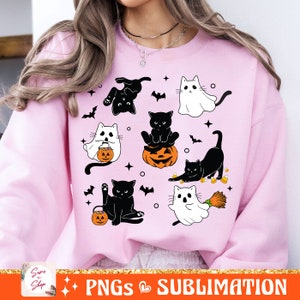 以下が含まれることがあります： 黒と白のハロウィーンのデザインが施されたピンクのトレーナー。猫、幽霊、コウモリ、カボチャ、コーンキャンディー、ほうきが描かれています。