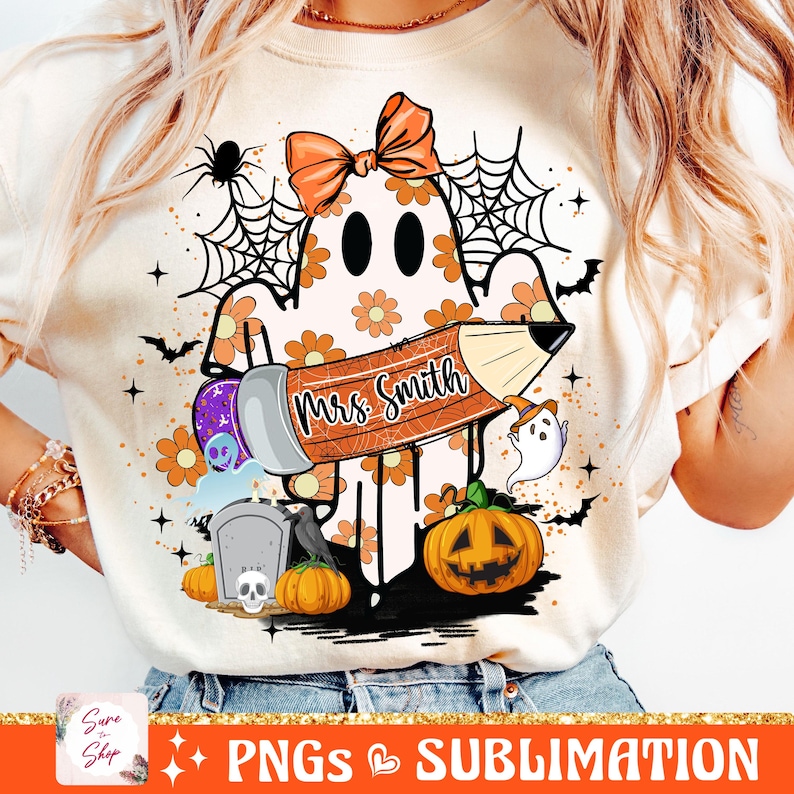 Puede incluir: Una camiseta blanca con un fantasma sosteniendo un l&aacute;piz que dice "Mrs. Smith". El fantasma est&aacute; decorado con flores naranjas y est&aacute; rodeado de elementos de tem&aacute;tica de Halloween como una telara&ntilde;a, murci&eacute;lagos y calabazas.