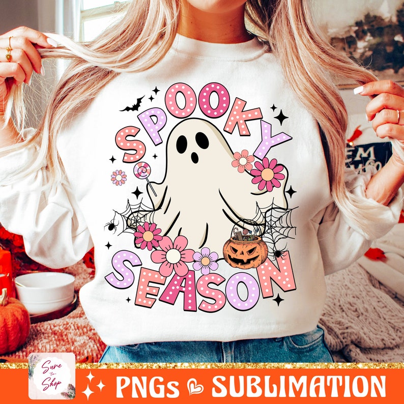 May include: A white sweatshirt with a pink and white graphic design that says "Spooky Season". The design features a ghost, a pumpkin, and flowers.