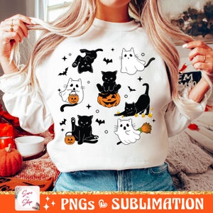 以下が含まれることがあります： 白地に黒と白のハロウィン猫と幽霊のデザインが施されたスウェットシャツ。デザインには、カボチャを持った猫、キャンディーを持った幽霊、ほうきを持った猫が描かれています。画像の下部には「PNGS SUBLIMATION」というテキストがあります。