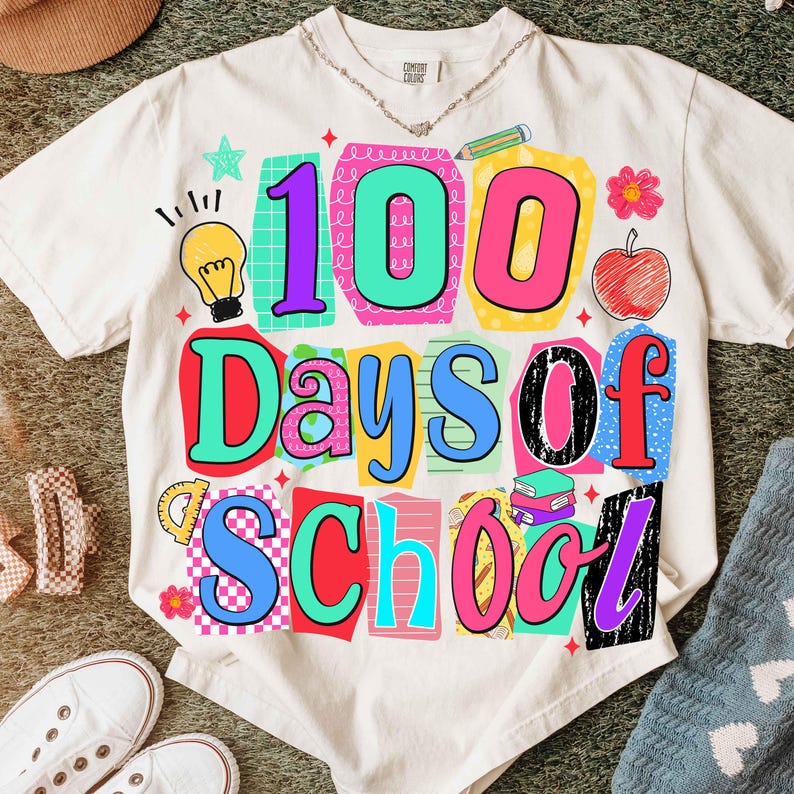 Puede incluir: Camiseta color crema con un gr&aacute;fico colorido que dice "100 Days of School". El dise&ntilde;o incluye una bombilla, una manzana, libros y otros elementos escolares en colores brillantes. La camiseta est&aacute; hecha de un material suave.