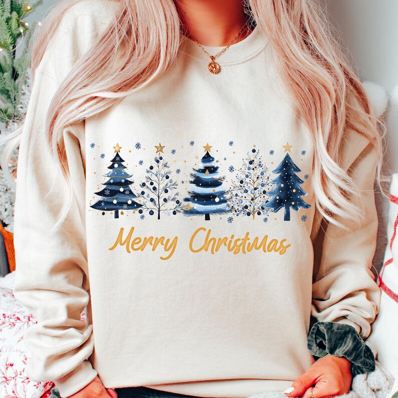 May include: A cream-colored sweatshirt with a festive design of blue and white Christmas trees and the text "Merry Christmas" in gold.
