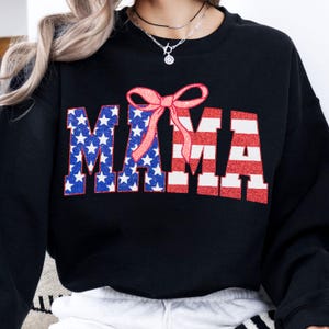 May include: Black sweatshirt with a red, white, and blue American flag design that says "MAMA" with a pink bow on top.