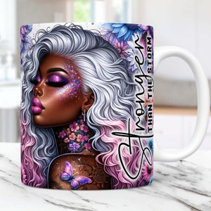 Könnte beinhalten: Weiße Keramiktasse mit einer farbenfrohen Illustration einer Frau mit silbernem Haar und rosa und violetten Highlights. Die Frau hat ein Schmetterlingstattoo auf ihrer Schulter und ist von Blumen umgeben. Der Text "Stronger than the storm" ist auf der Tasse geschrieben.