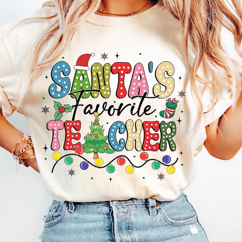 May include: A white t-shirt with a colorful graphic that says "Santa's Favorite Teacher" with a Christmas tree, lights, and a stocking.