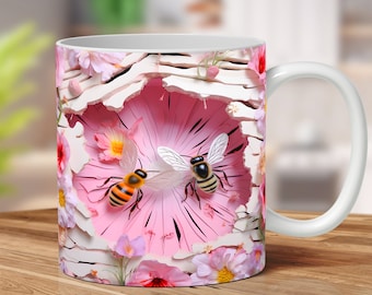 May include: White ceramic mug with a pink and white floral design featuring two bees. The bees are flying in front of a pink flower with white petals.