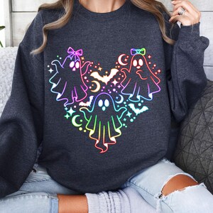 May include: A dark gray sweatshirt with a rainbow-colored design of three ghosts with bows and bats. The ghosts are arranged in a heart shape.