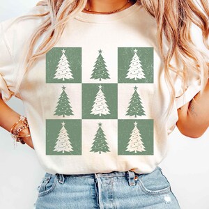 May include: A white t-shirt with a green and white checkered pattern featuring a repeating design of stylized Christmas trees.