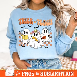 May include: A light blue sweatshirt featuring a design of three ghosts. The ghosts are holding a book, a pencil, and a pumpkin. The text "Trick or Teach" is above the ghosts.