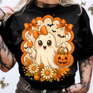 Pode incluir: Camiseta preta com um fantasma de desenho animado segurando doces e uma lanterna de ab&oacute;bora. O design inclui la&ccedil;os laranja, morcegos, flores e folhas de outono, dentro de uma borda ondulada.