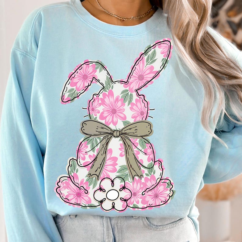 May include: Light blue sweatshirt with a floral bunny design. The bunny is pink and green with a brown bow.