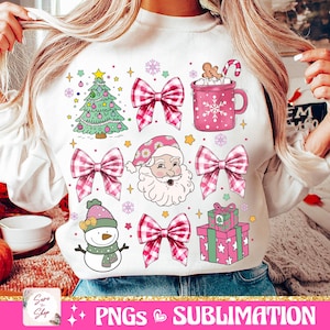 May include: White sweatshirt with a pink and white Christmas design. The design includes a Christmas tree, Santa Claus, a snowman, presents, bows, and a mug of hot chocolate.
