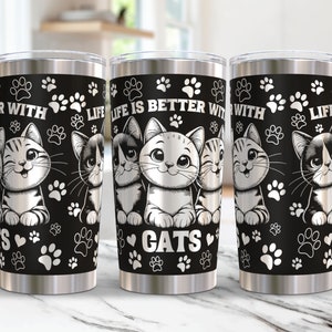 Puede incluir: Vaso de acero inoxidable con fondo negro, huellas de patas blancas y la frase "LIFE IS BETTER WITH CATS". El vaso muestra ilustraciones de gatos sonrientes en varias poses.