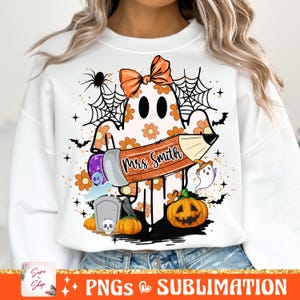 Puede incluir: Una sudadera blanca con un fantasma que lleva un lazo y sostiene un l&aacute;piz que dice "Mrs. Smith". El fantasma est&aacute; rodeado de im&aacute;genes de tem&aacute;tica de Halloween, incluyendo calabazas, murci&eacute;lagos y telara&ntilde;as.