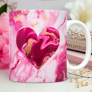 May include: White ceramic mug with a pink and white marble design. A heart-shaped cutout reveals a darker pink interior with gold accents. The mug has a white handle and is suitable for hot or cold beverages.