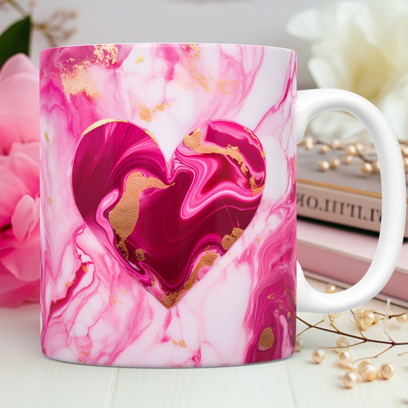 May include: White ceramic mug with a pink and white marble design. A heart-shaped cutout reveals a darker pink interior with gold accents. The mug has a white handle and is suitable for hot or cold beverages.