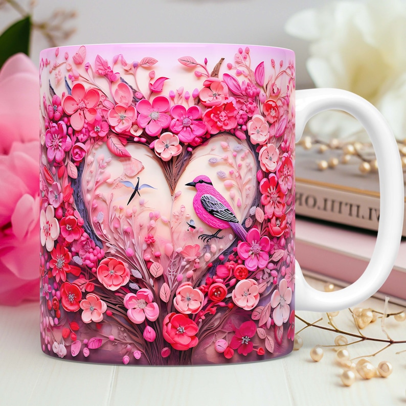 May include: White ceramic mug featuring a heart-shaped floral design with a pink bird. The design includes various shades of pink flowers and leaves, with a white handle. The mug is decorated with a 3D effect.