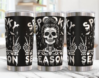 Op de afbeelding: Drie roestvrijstalen bekers met een zwarte achtergrond en een wit ontwerp. Het ontwerp bevat een skelet met een knot in het haar, vredestekens en de tekst "Spooky Season".