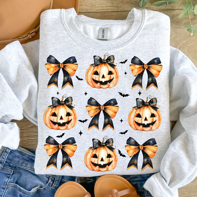 May include: A gray sweatshirt with a repeating pattern of orange pumpkins with black eyes and a toothy grin, each with a black and orange bow on top.  The pumpkins are surrounded by small black bats.