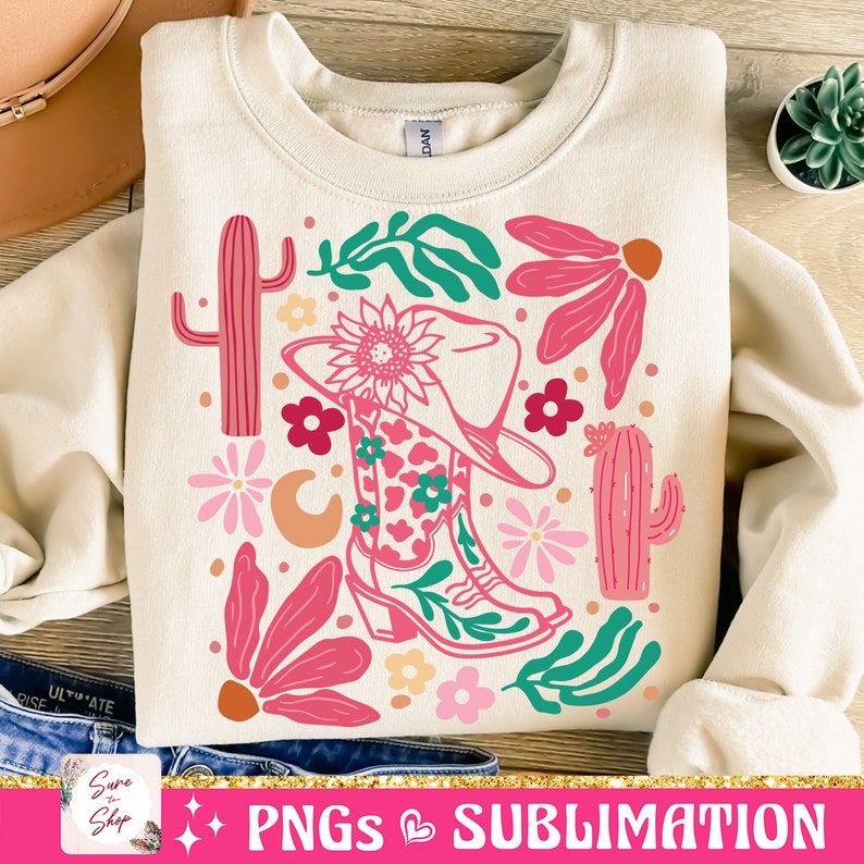 May include: Cream-colored sweatshirt with a vibrant graphic featuring a cowboy boot, hat, cacti, and floral elements in pink, green, and peach. The design includes the text "PNGs Sublimation" at the bottom.