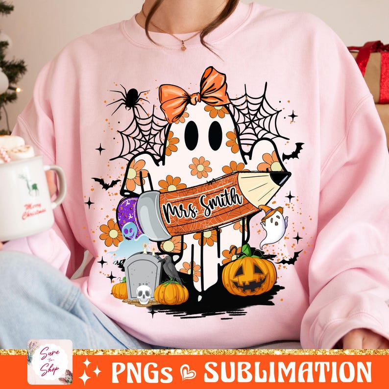 Puede incluir: Sudadera rosa con un fantasma sosteniendo un l&aacute;piz que dice "Mrs. Smith" con un lazo en la cabeza. El fantasma est&aacute; rodeado de calabazas, murci&eacute;lagos y telara&ntilde;as.