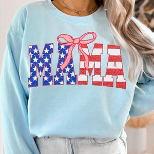 May include: Light blue sweatshirt with a red, white, and blue American flag design that spells out "MAMA" with a pink bow on top.