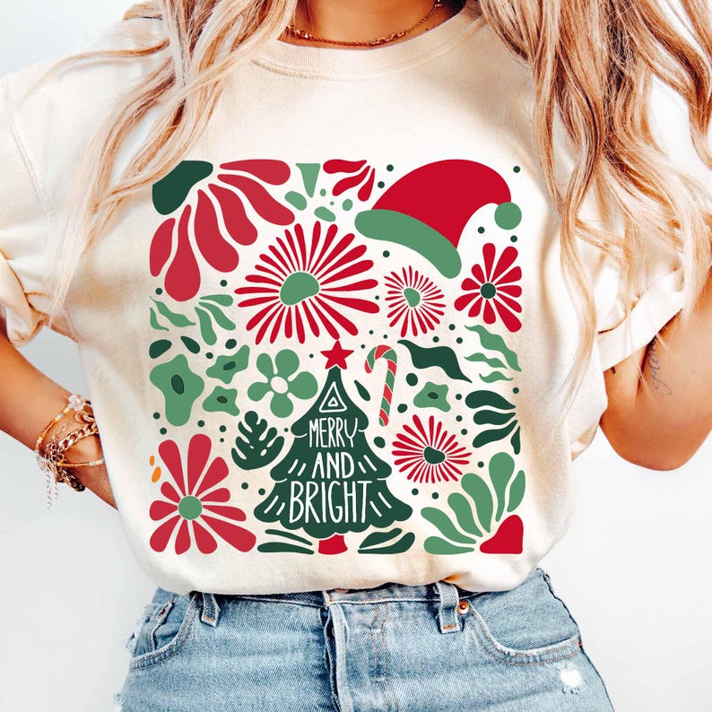 Puede incluir: Sudadera de color crema con un dise&ntilde;o navide&ntilde;o festivo. El gr&aacute;fico incluye elementos florales rojos y verdes, un gorro de Pap&aacute; Noel, un bast&oacute;n de caramelo y un &aacute;rbol de Navidad con las palabras "MERRY AND BRIGHT".
