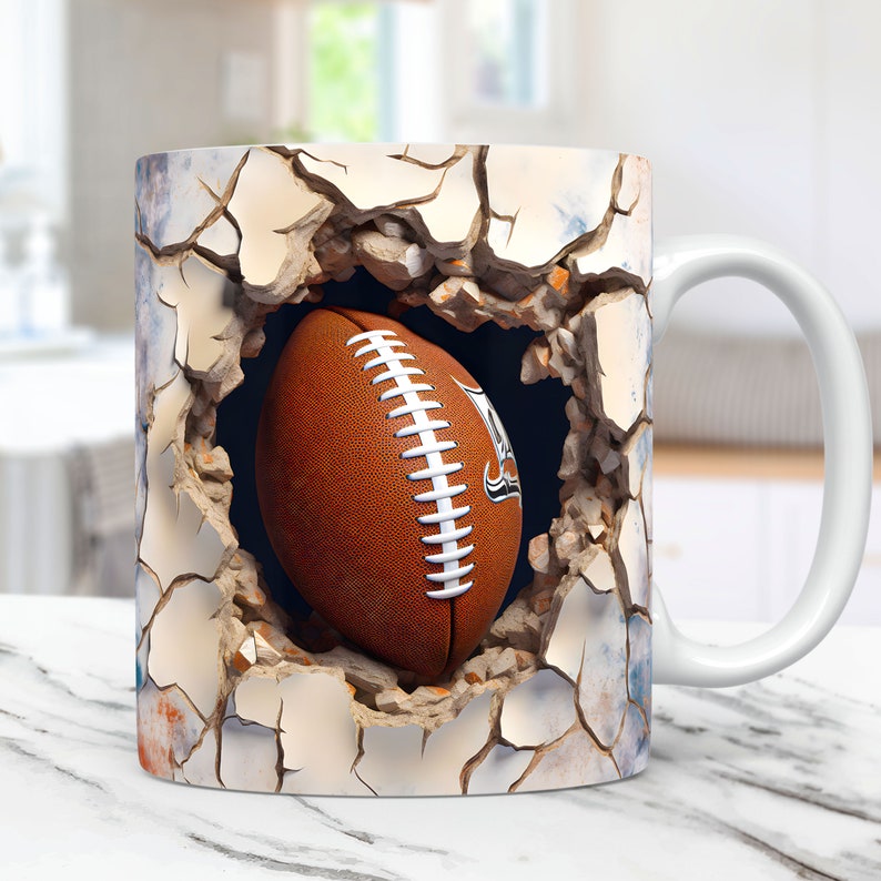 May include: White ceramic mug with a graphic of a football breaking through a cracked wall. The football is brown and white with a black and white logo.