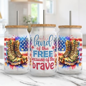 K&ouml;nnte beinhalten: Drei Glasbecher mit Holzdeckeln und Metallstrohhalmen. Jeder Becher hat ein Design mit der amerikanischen Flagge, Milit&auml;rstiefeln und dem Text "Land of the Free because of the Brave" in Rot und Blau.