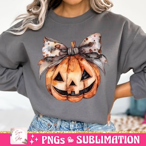 May include: A gray sweatshirt with a watercolor pumpkin with a brown and white polka dot bow. The pumpkin has a jack-o-lantern face.