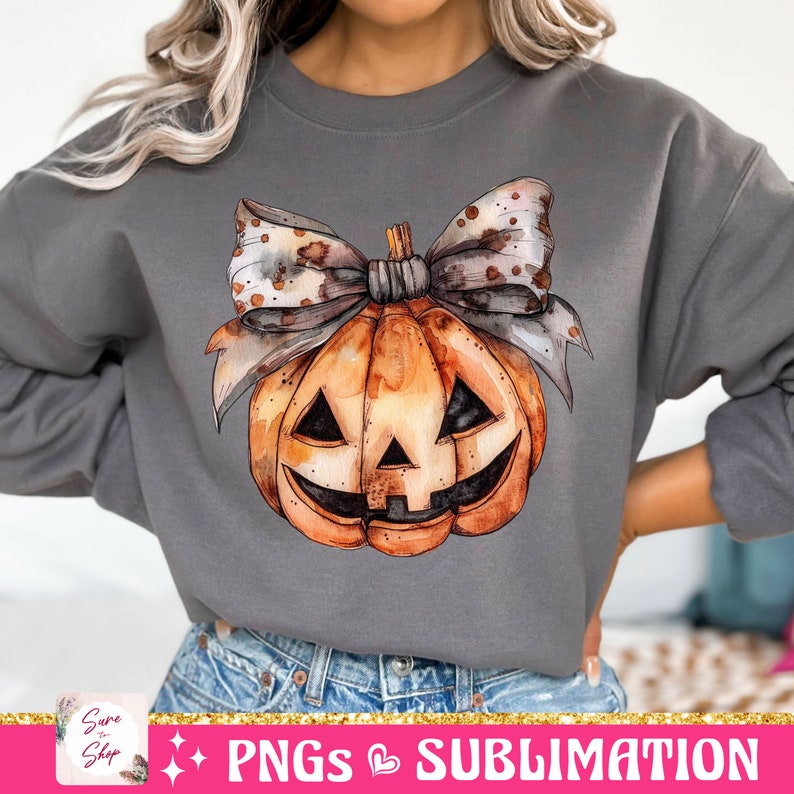 May include: A gray sweatshirt with a watercolor pumpkin with a brown and white polka dot bow. The pumpkin has a jack-o-lantern face.