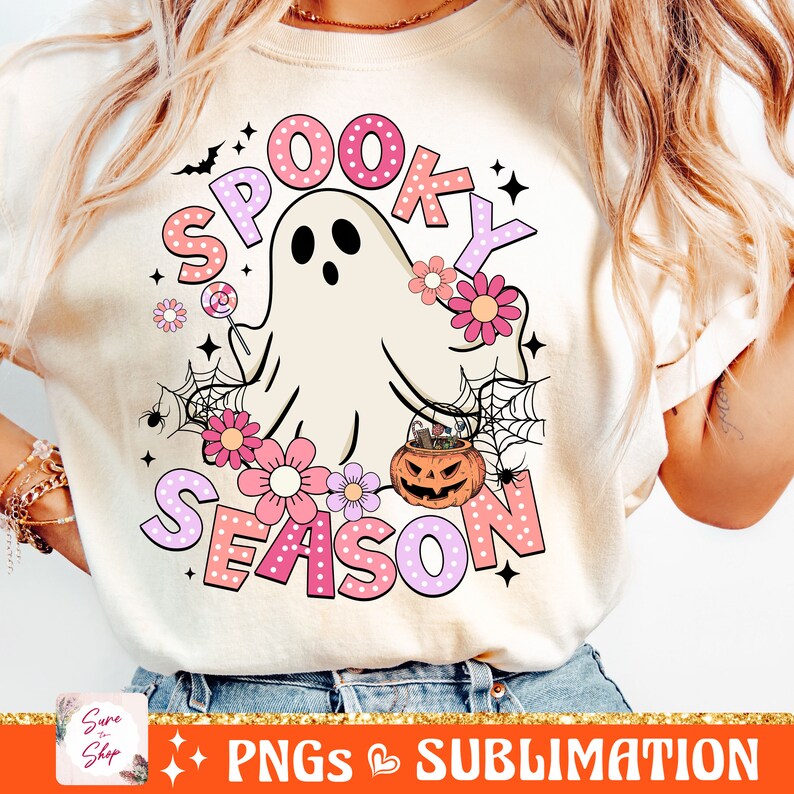 May include: A white t-shirt with a pink and white graphic design featuring a ghost, flowers, a pumpkin, and the text "Spooky Season".