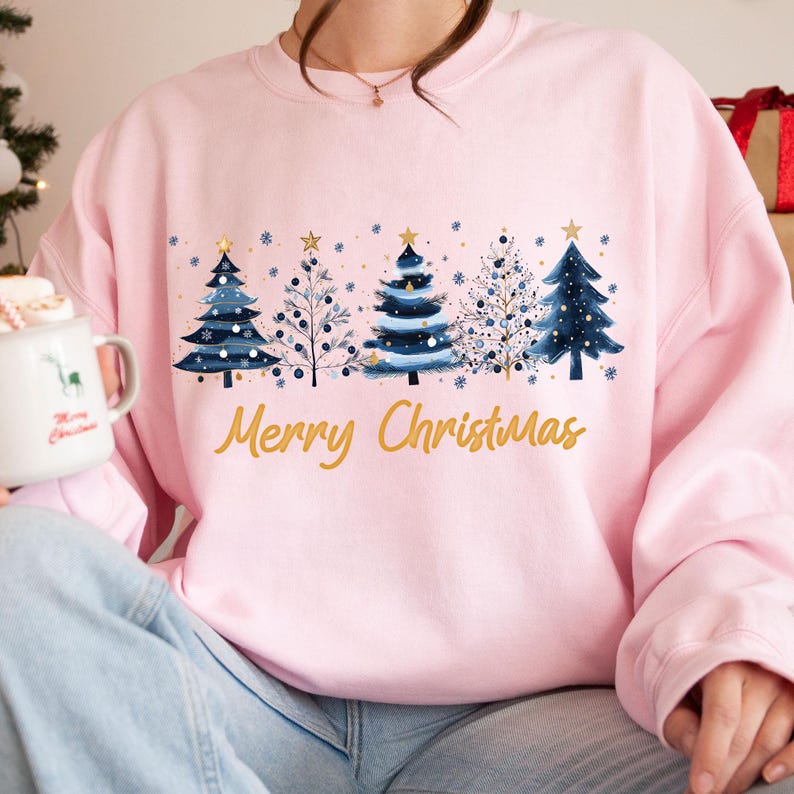 May include: Pink sweatshirt with a blue and gold Christmas tree design and the text "Merry Christmas".