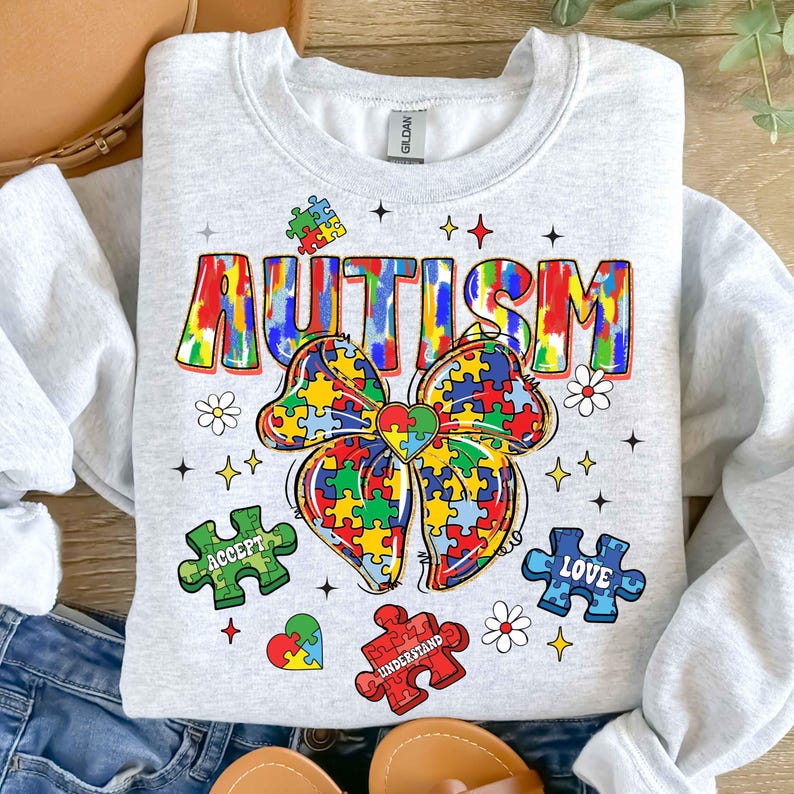 May include: A gray sweatshirt with a colorful tie-dye design that says "AUTISM" with a puzzle piece bow and the words "ACCEPT", "UNDERSTAND", and "LOVE" on puzzle pieces.