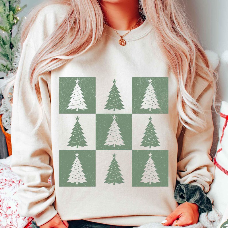 May include: A cream-colored sweatshirt with a pattern of nine green and white Christmas trees. The trees are arranged in a grid pattern.