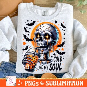 May include: A gray sweatshirt with a graphic of a skeleton drinking a cold beverage. The skeleton has glowing eyes and is dripping with a liquid that looks like orange juice. The text "Cold Like My Soul" is printed below the skeleton. The background is orange with bats and stars.