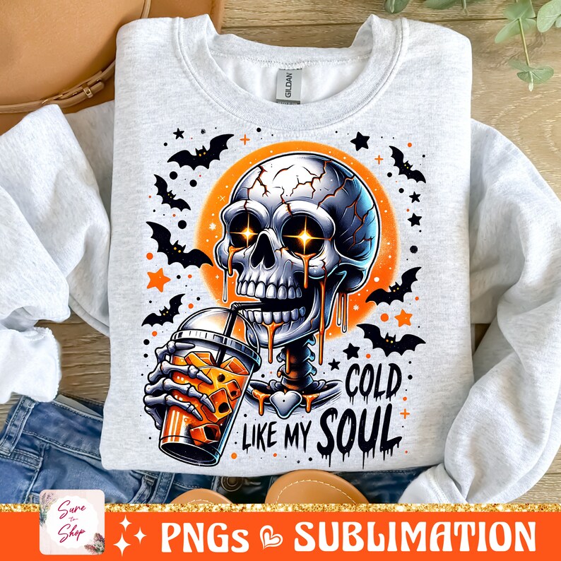 May include: A gray sweatshirt with a graphic of a skeleton drinking a cold beverage. The skeleton has glowing eyes and is dripping with a liquid that looks like orange juice. The text "Cold Like My Soul" is printed below the skeleton. The background is orange with bats and stars.