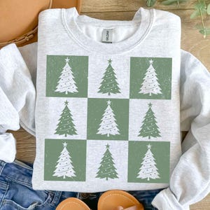 May include: A gray sweatshirt with a green and white Christmas tree pattern. The trees are arranged in a checkered pattern on the sweatshirt.