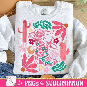 May include: A light gray sweatshirt featuring a colorful graphic design. The design includes a cowboy boot, hat, cacti, flowers, and leaves in shades of pink, green, and orange. The text "PNGs Sublimation" is at the bottom.
