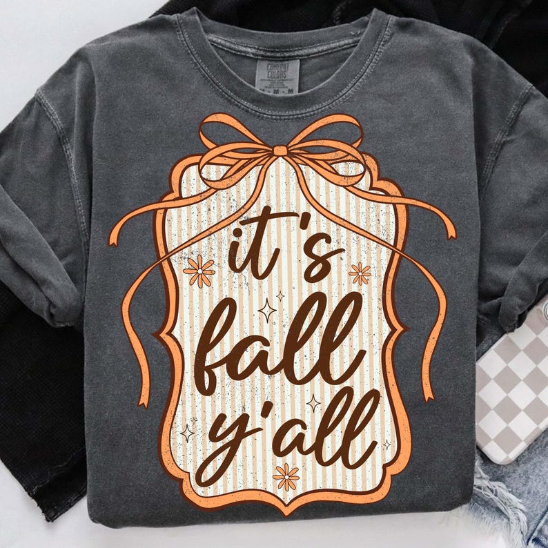May include: Dark gray sweatshirt with a decorative orange and white graphic that reads "it's fall y'all". The graphic has a bow and floral accents. The sweatshirt is a comfortable, casual style.