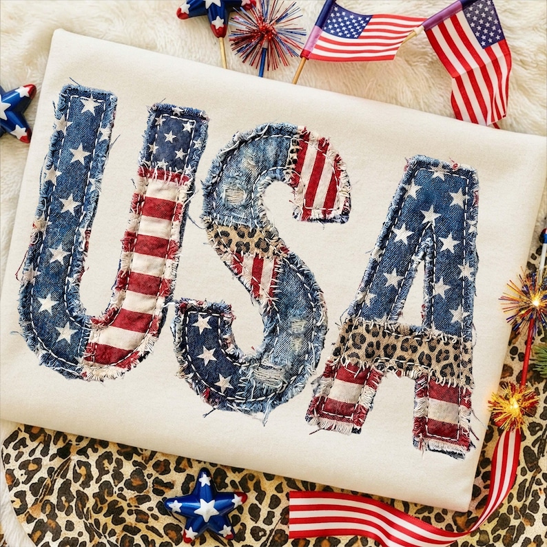 Pu&ograve; includere: Una maglietta color crema con la scritta "USA" applicata in denim, strisce della bandiera americana e stampa leopardata. Le lettere sono cucite con filo bianco, un design patriottico.